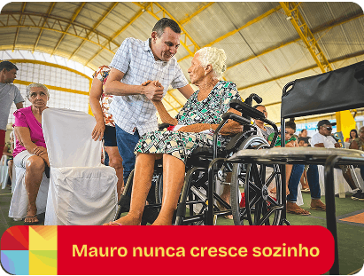 Mauro Eduardo apoiando uma senhora cadeirante em um evento. Legenda: Mauro nunca cresce sozinho